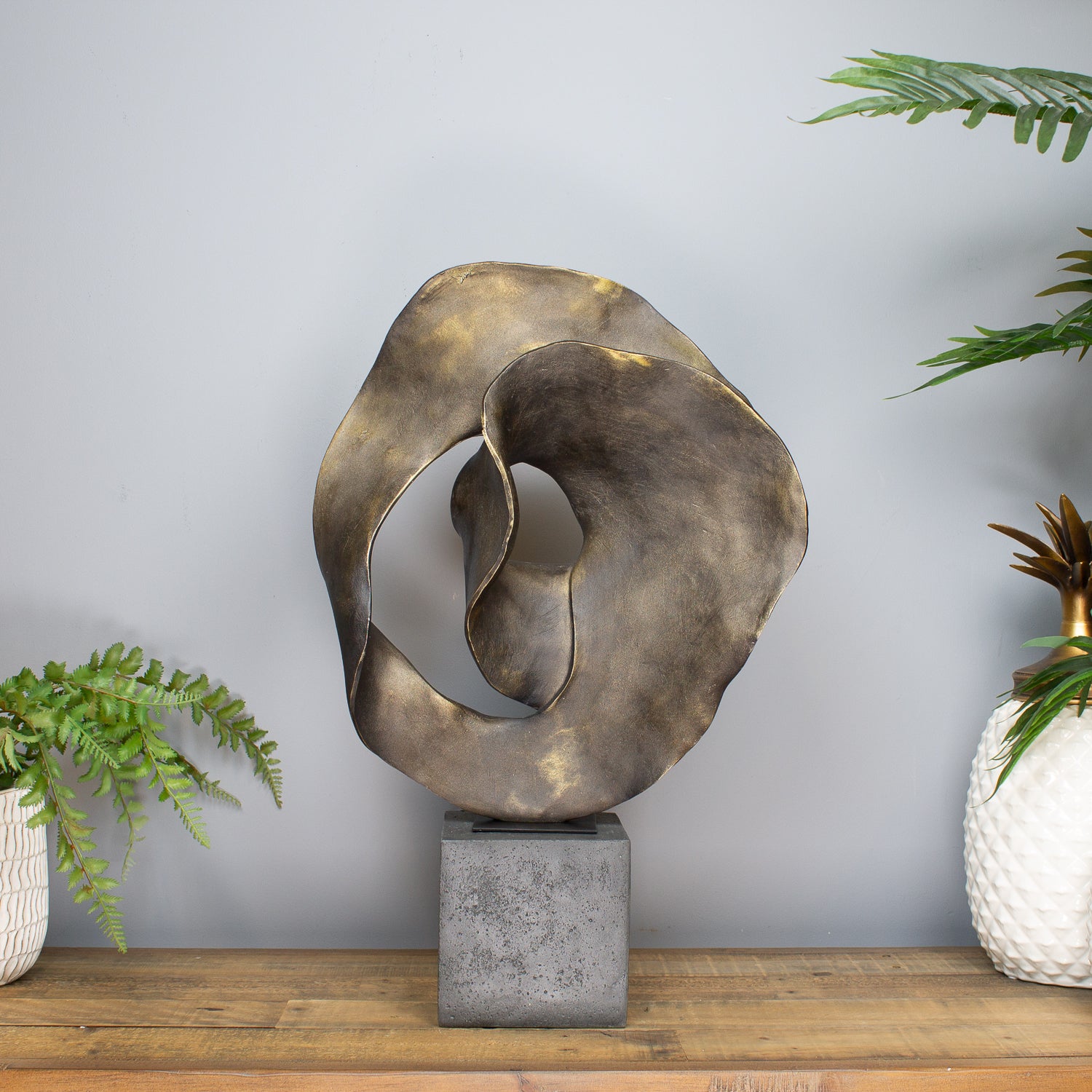 Abstract metal sculpture on a wooden surface with plants in the background