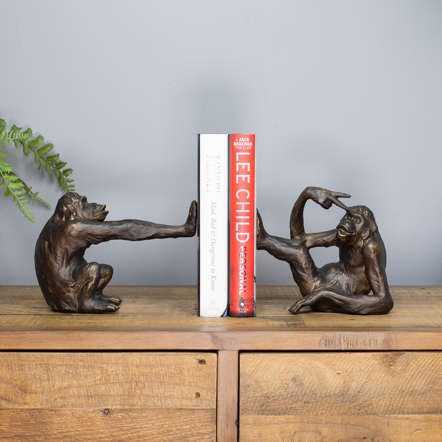 Bronze monkey bookends holding a book on a wooden surface with a gray background