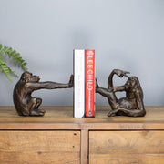 Bronze monkey bookends holding a book on a wooden surface with a gray background
