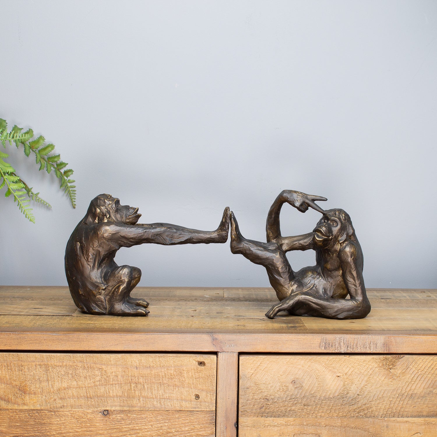 Bronze monkey sculptures on a wooden surface with a light gray background