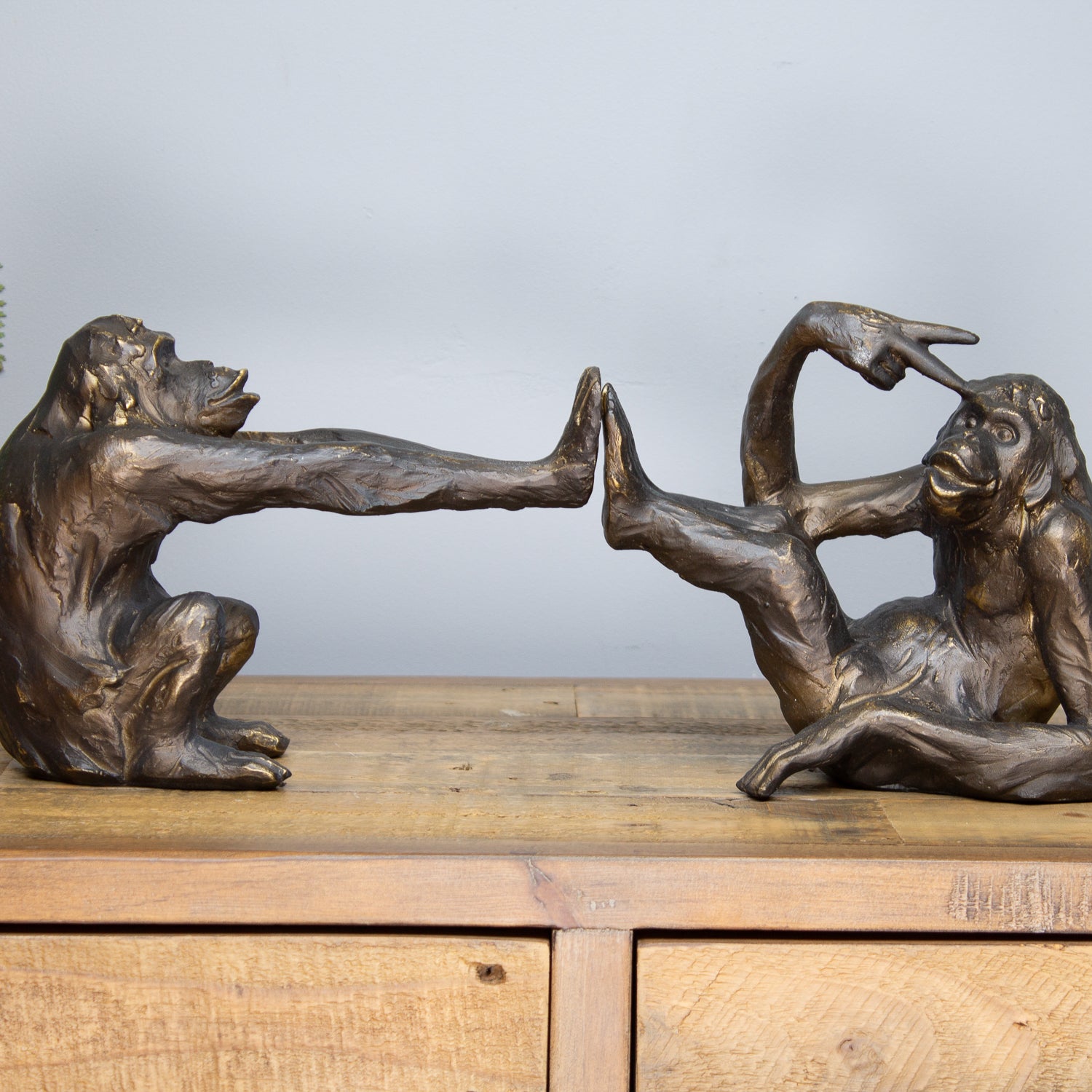 Bronze monkey sculptures on a wooden surface with a neutral background