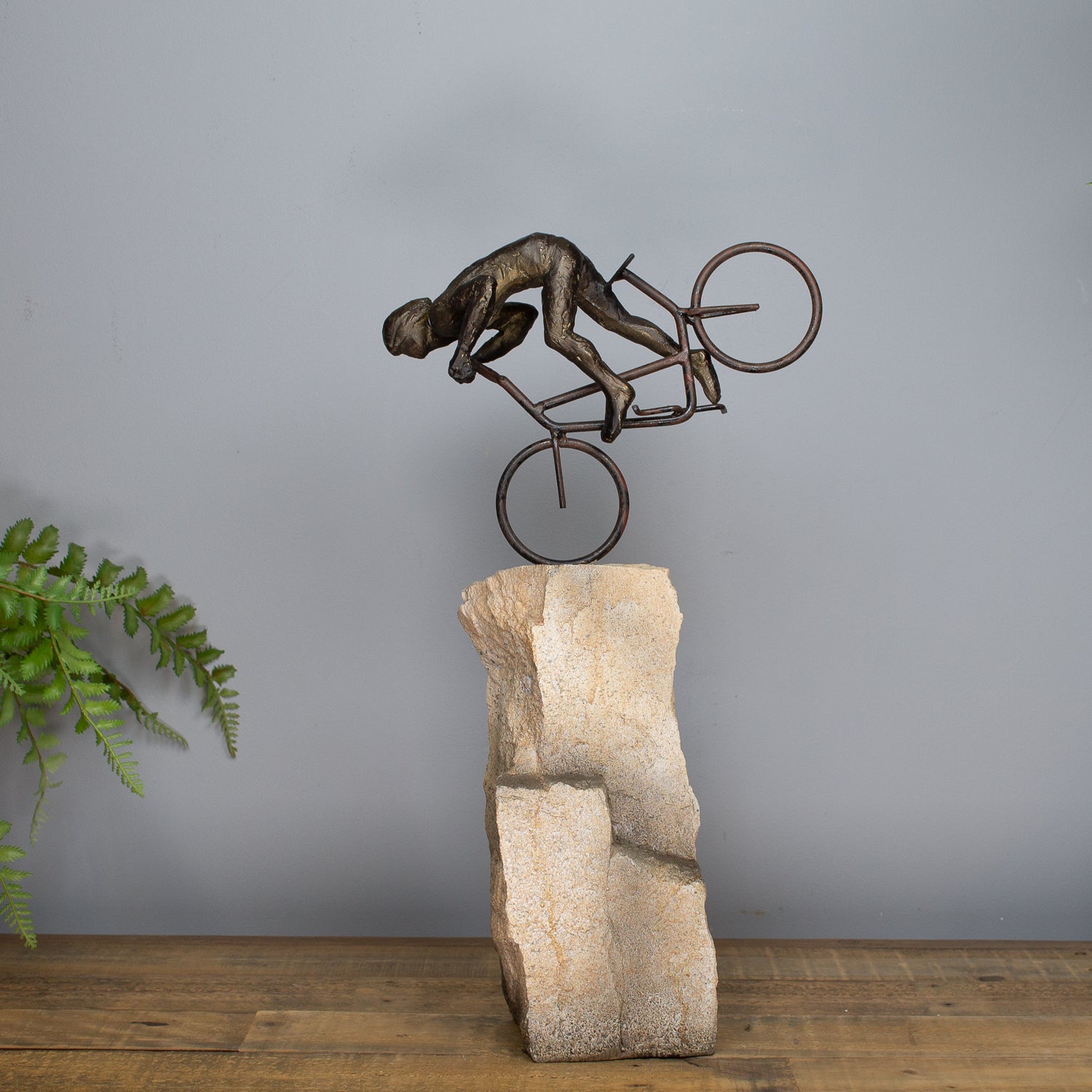 Bronze sculpture of a cyclist on a rock pedestal against a gray wall