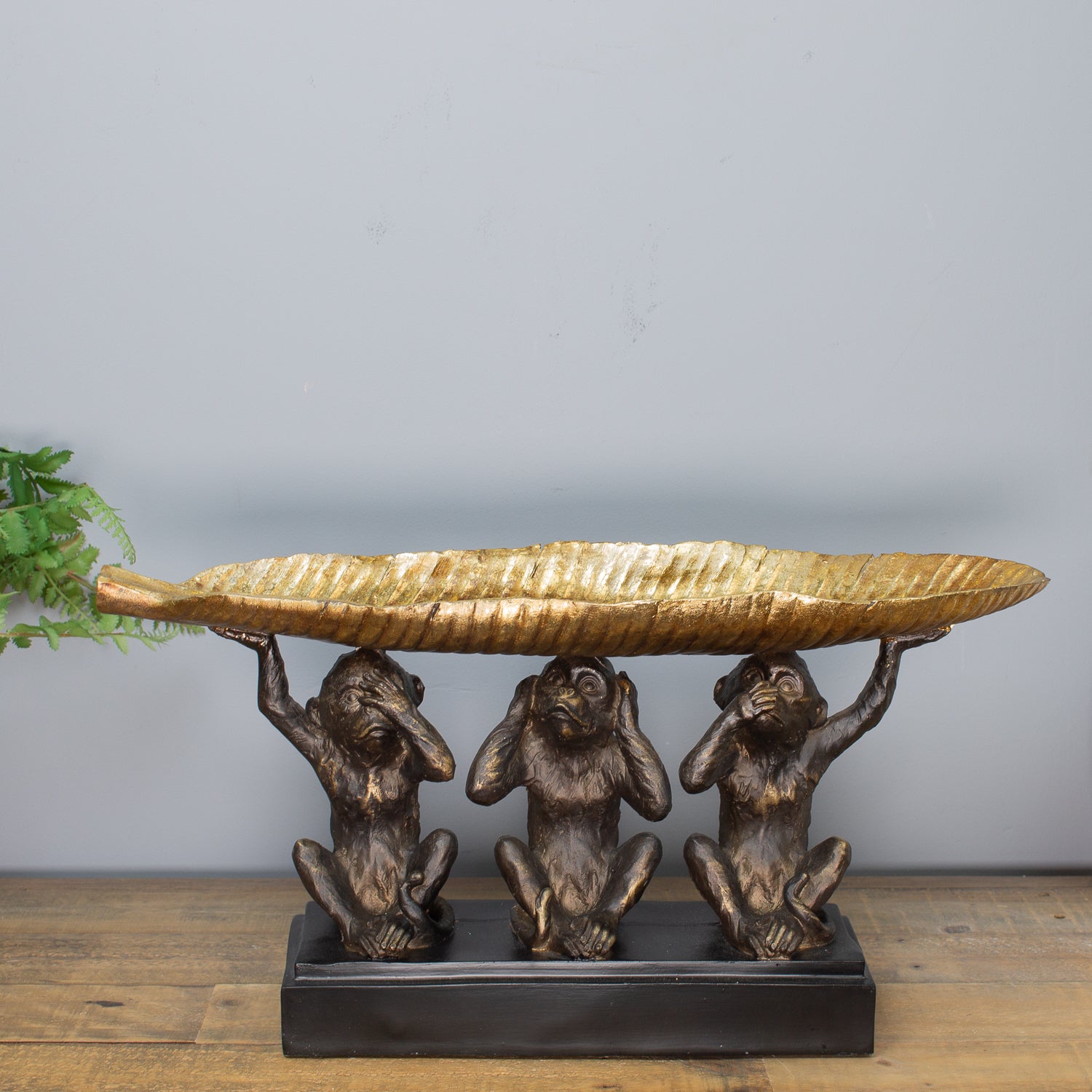 Decorative sculpture of three monkeys holding a leaf tray on a plain background