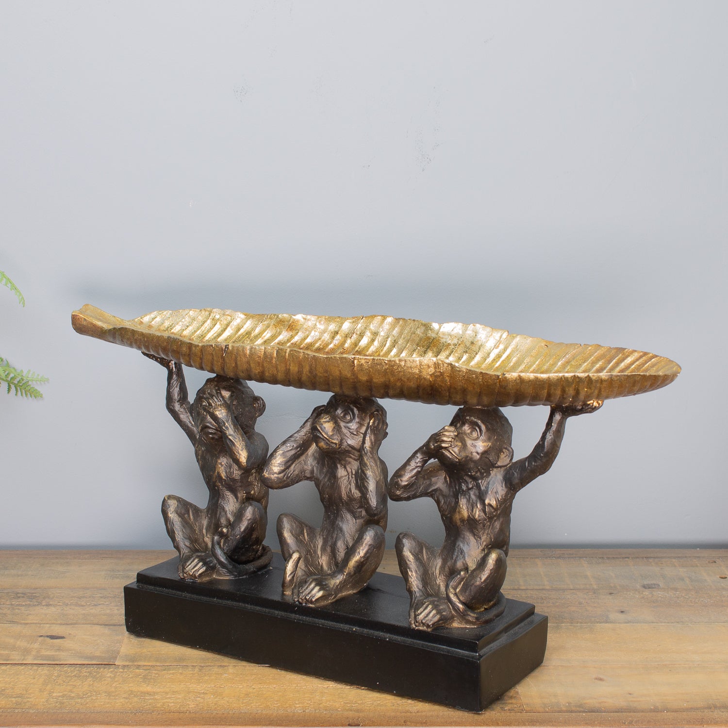 Bronze sculpture of three monkeys holding a leaf on a wooden surface with a gray background