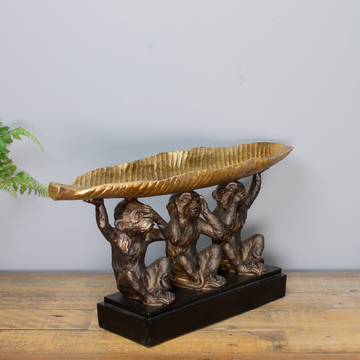 Bronze sculpture of three monkeys holding a leaf on a wooden surface with a gray background