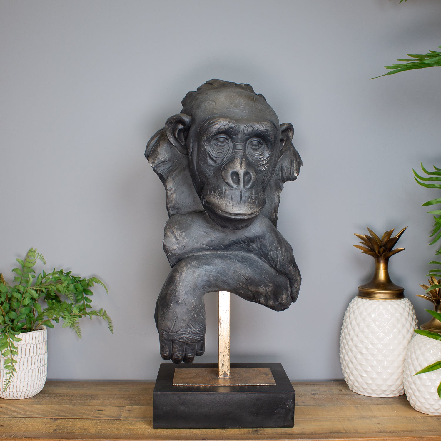 Statue of a monkey on a stand with decorative plants in the background