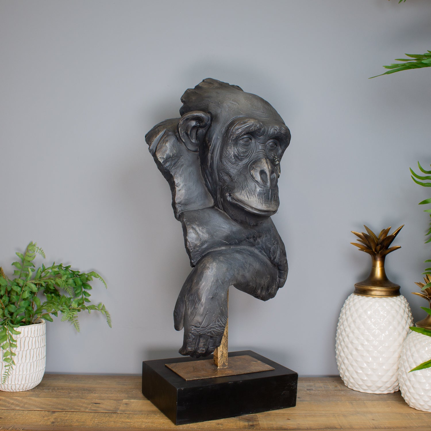 Bronze statue of a monkey on a wooden base with decorative plants in the background
