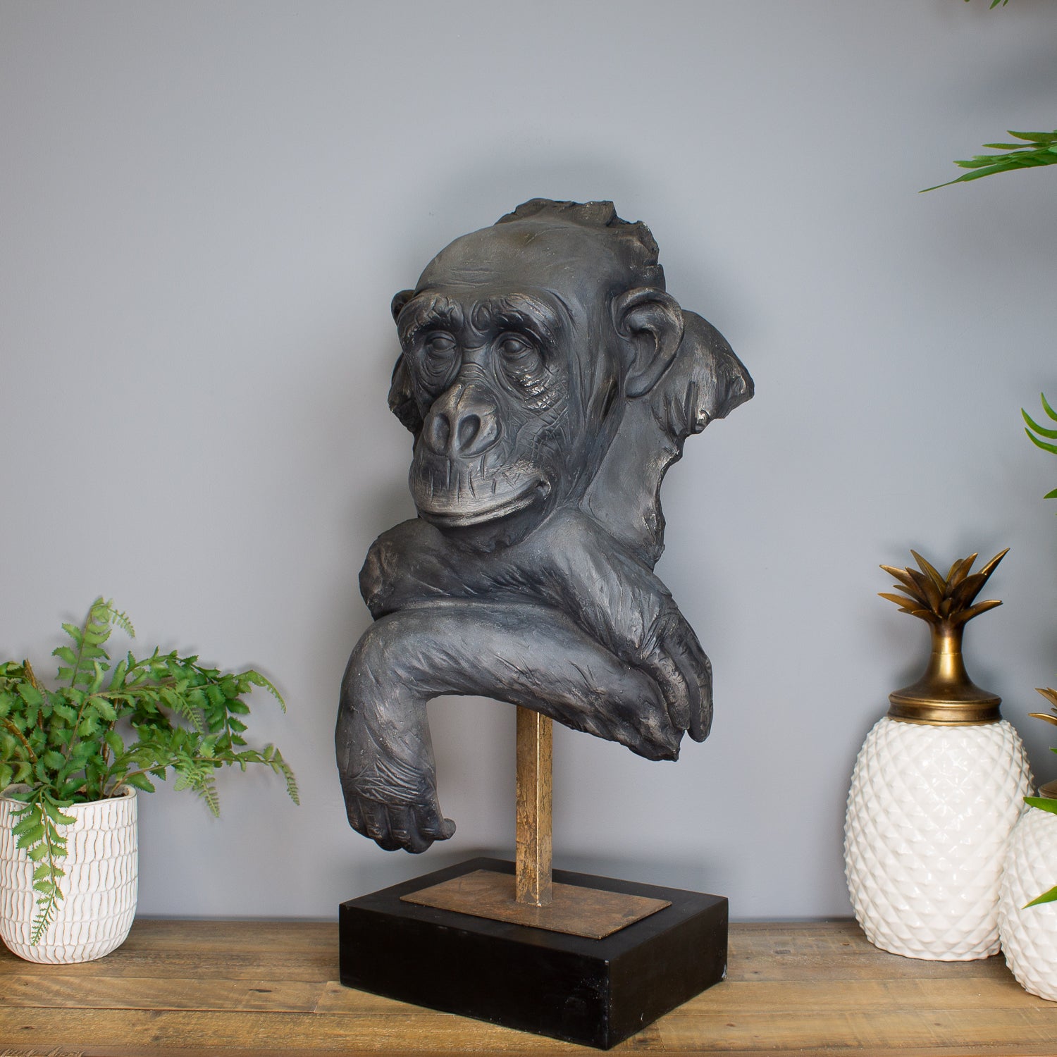 Gorilla head sculpture on a stand with decorative plants and pineapple in the background