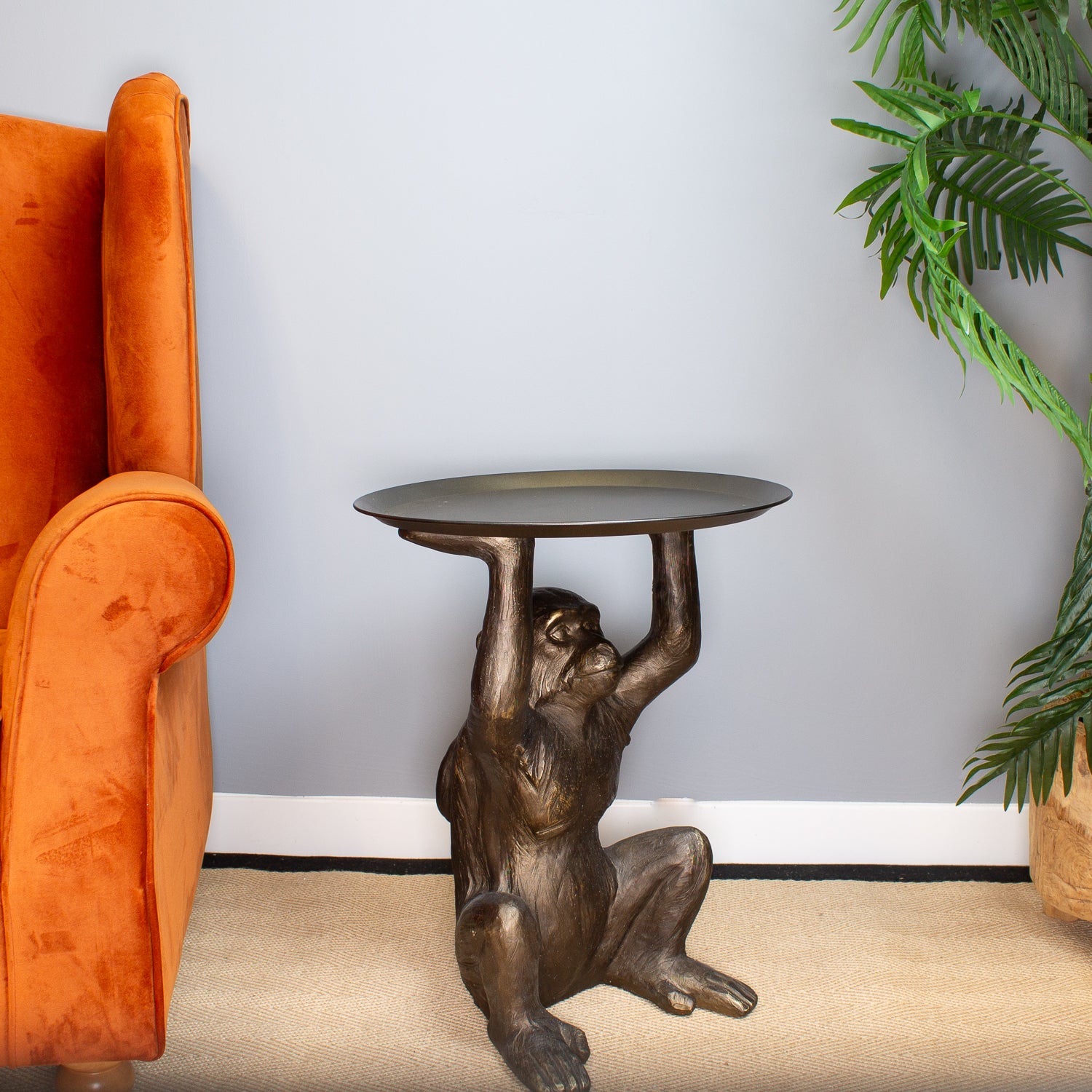 Bronze monkey table with a round top in a room with an orange chair and a plant.