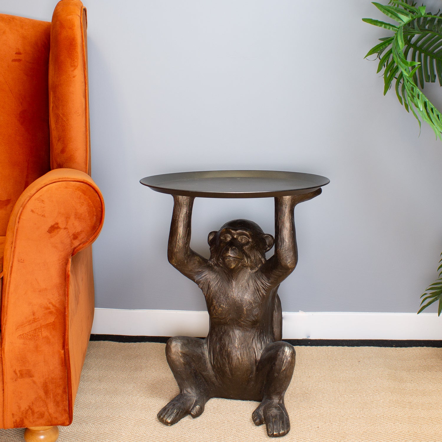 Bronze monkey table with a round top in a room with an orange armchair and a plant.
