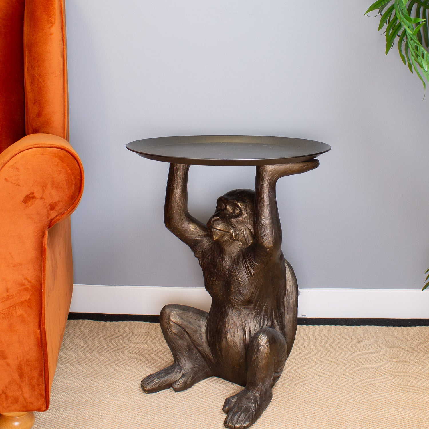 Bronze monkey table with a round top, placed against a neutral wall.