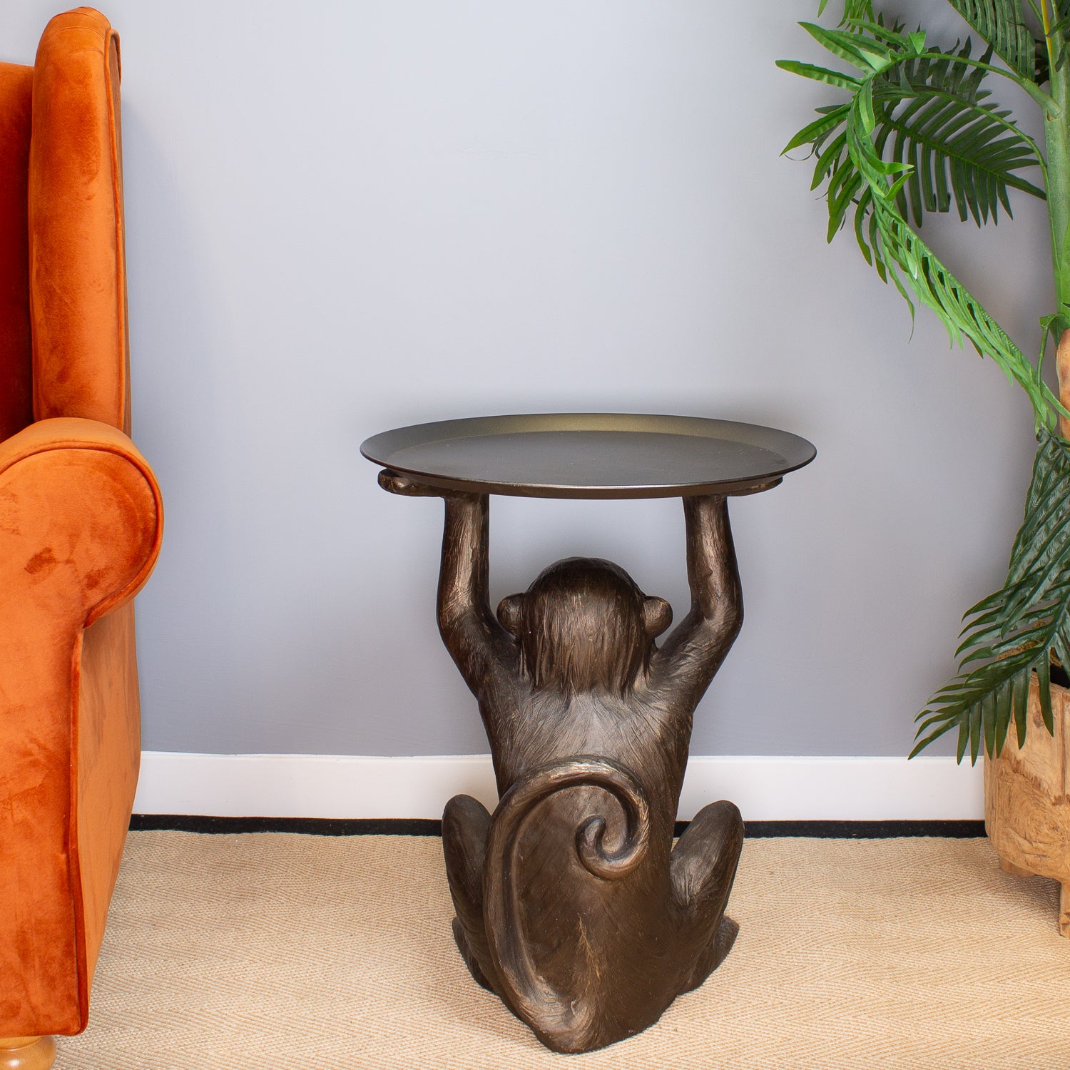Bronze monkey table with a round top in a room with an orange chair and a plant.