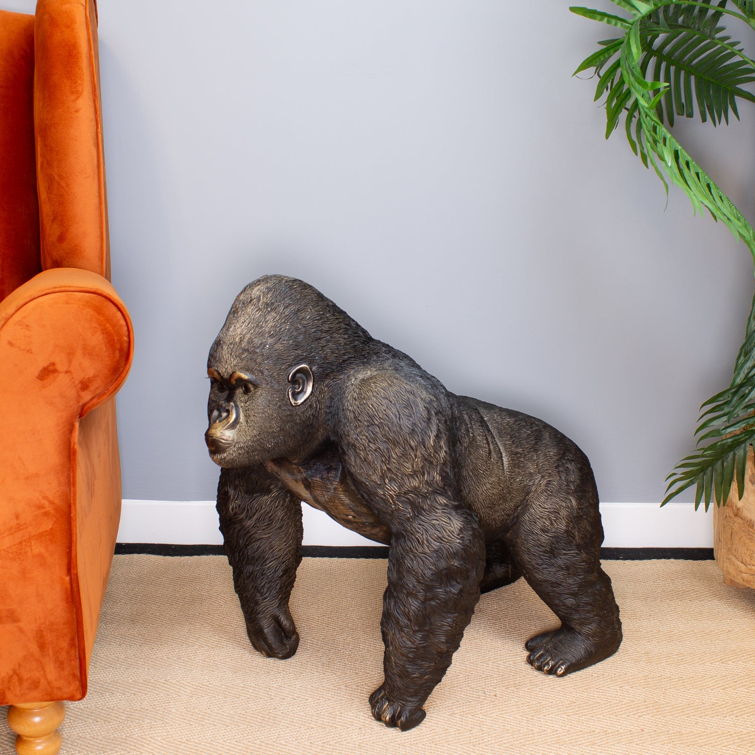 Gorilla statue on a beige carpet next to an orange armchair with a plant in the background.