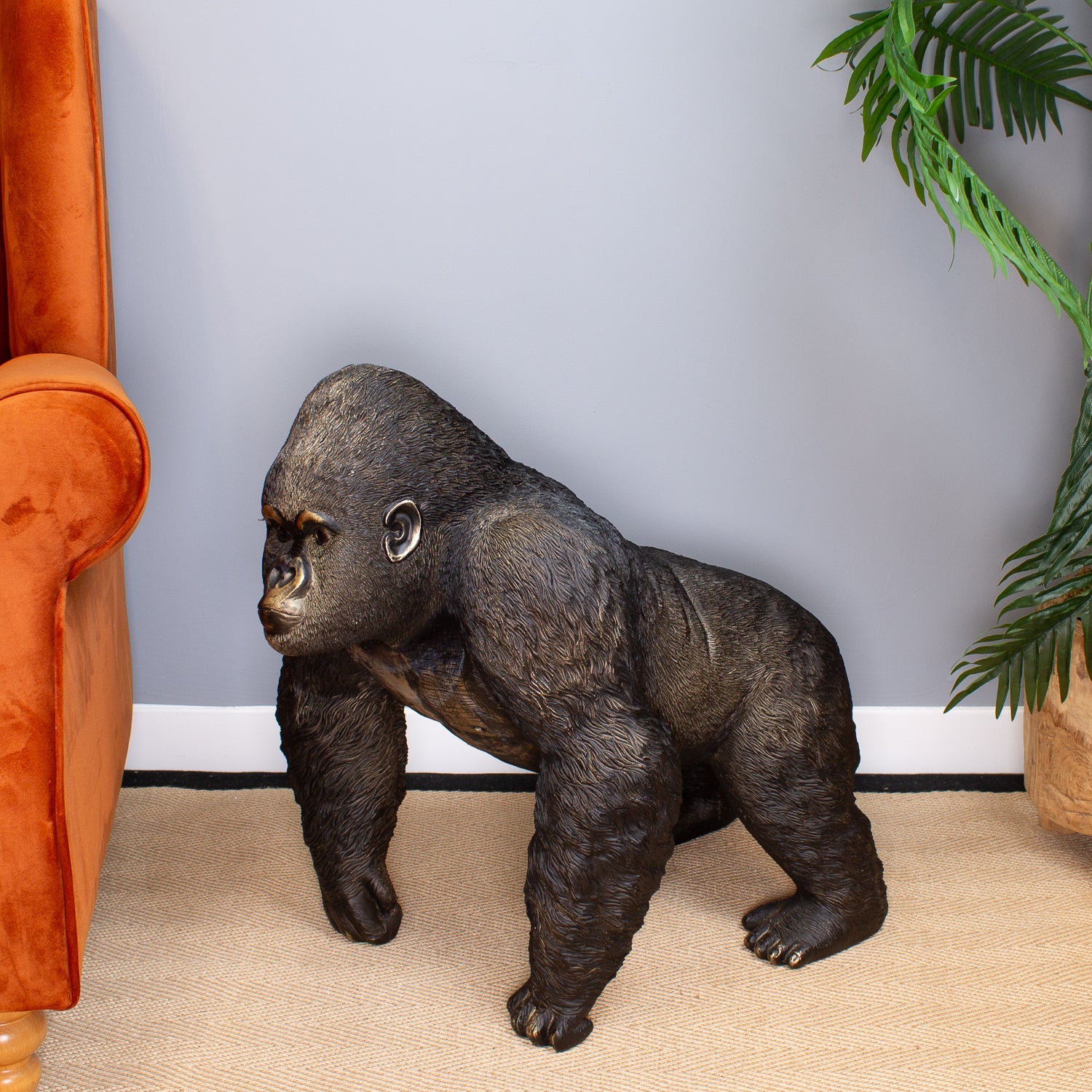 Statue of a gorilla in a room with an orange chair and plant