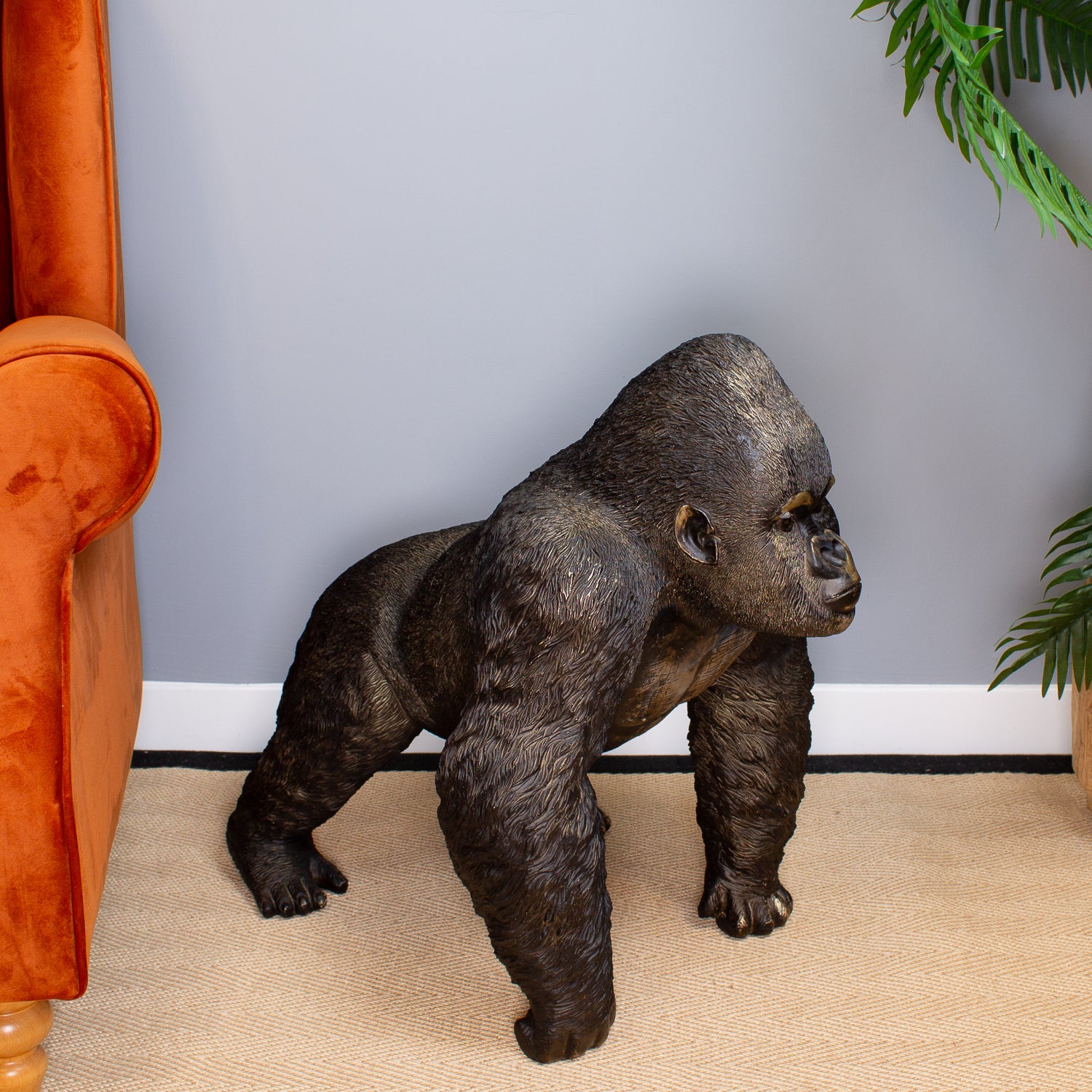 Statue of a gorilla in a room with an orange chair and gray wall.