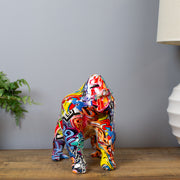 Colorful gorilla statue on a wooden surface with a gray wall and plant in the background